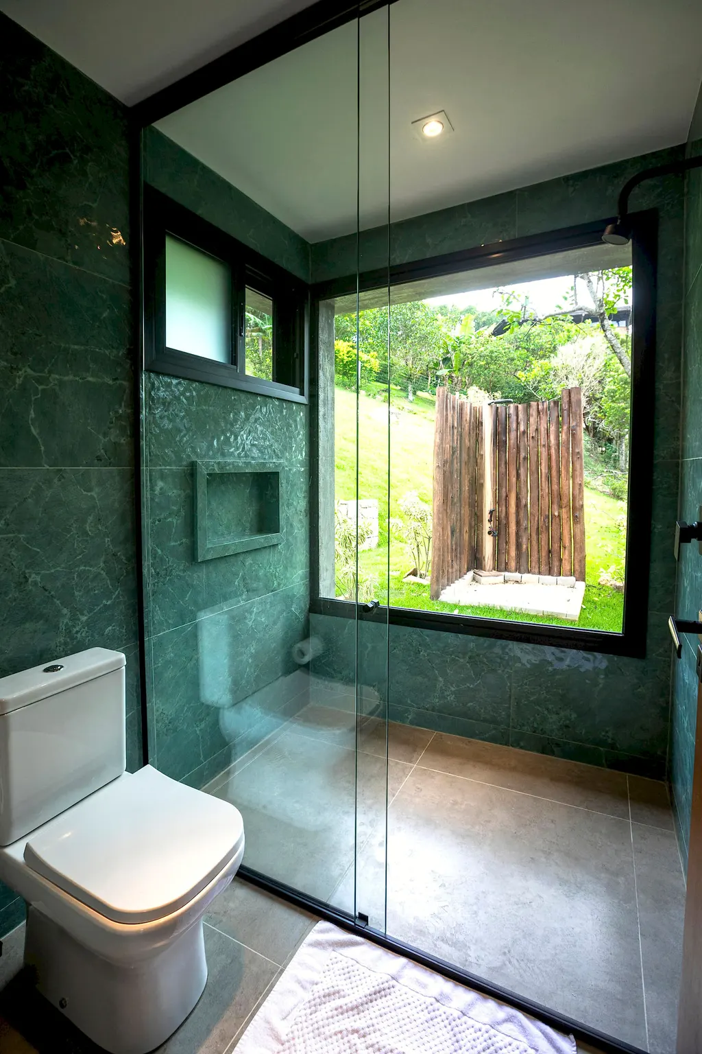 Banheiro verde com vista para o chuveiro externo no jardim