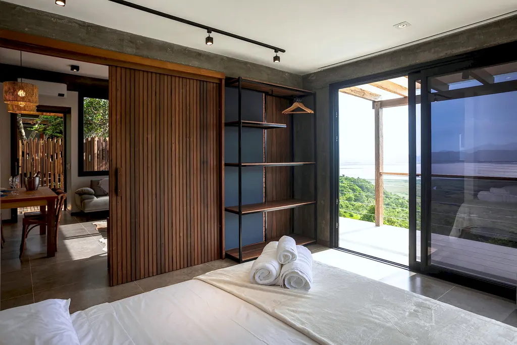 Quarto do Espaço Lagoa com painel de madeira e porta de vidro para o deck