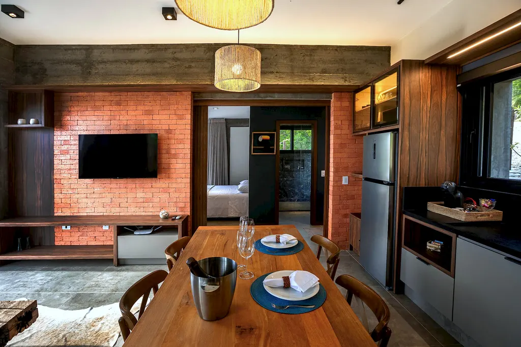 Sala de jantar com parede de tijolos, TV e cozinha ao fundo