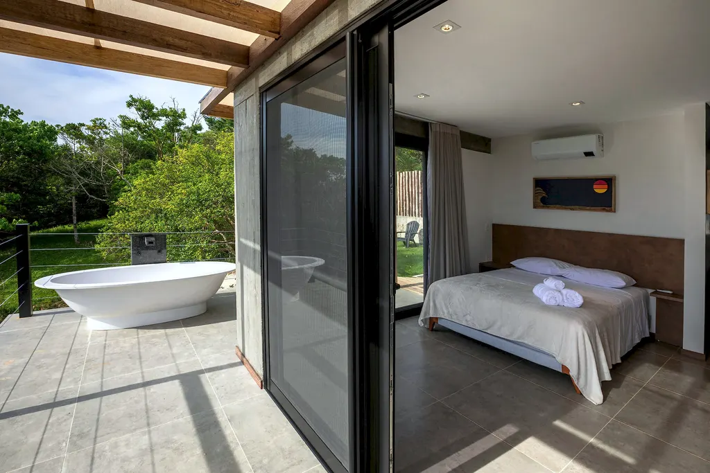 Quarto e banheira externa lado a lado, separados por porta de vidro