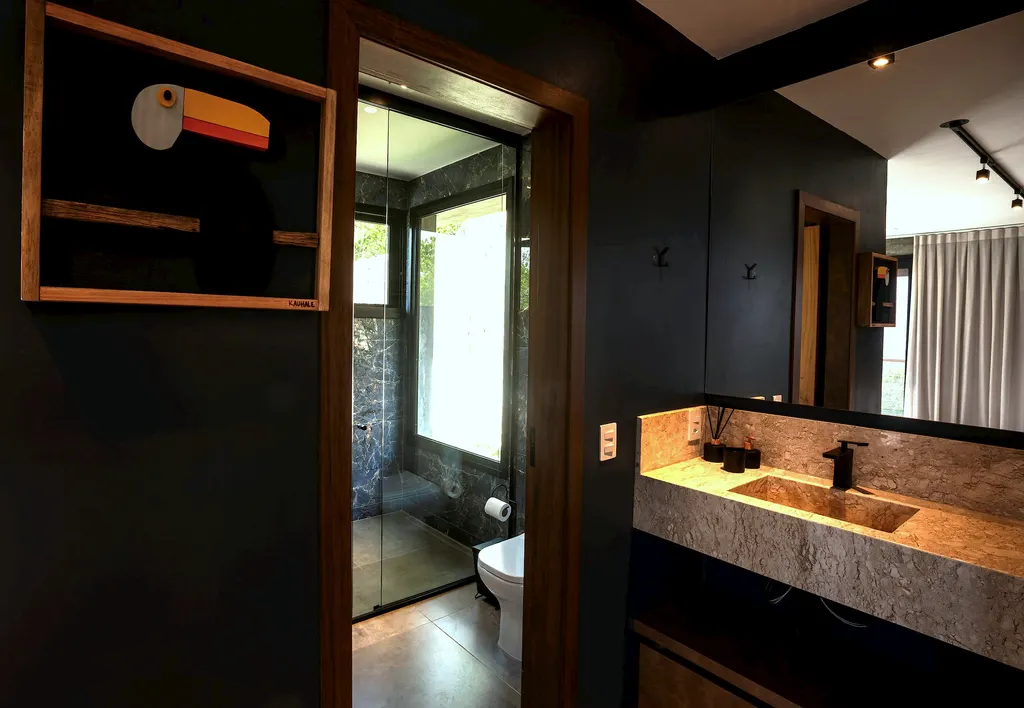 Lavabo com bancada de pedra, iluminação quente e quadro de tucano