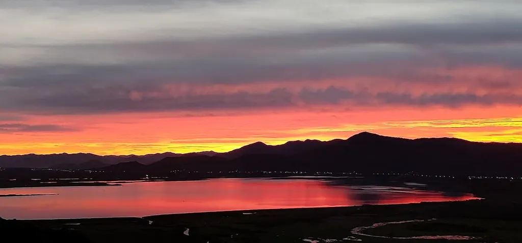Pôr do sol alaranjado atrás da serra, refletido na lagoa, visto do Refúgio da Silveira